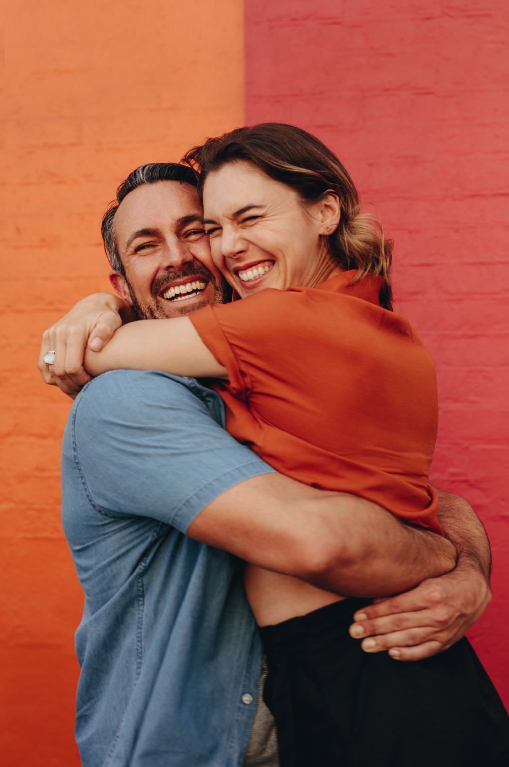 Loving middle aged couple embracing against colored wall. Mature man and woman together against red and orange wall.