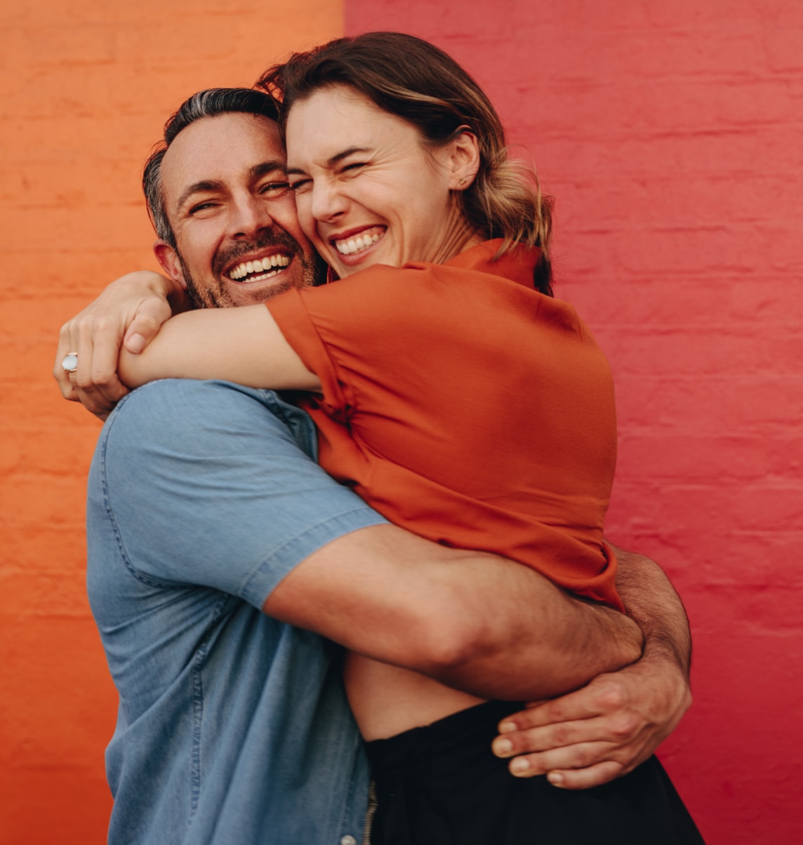 Loving middle aged couple embracing against colored wall. Mature man and woman together against red and orange wall.