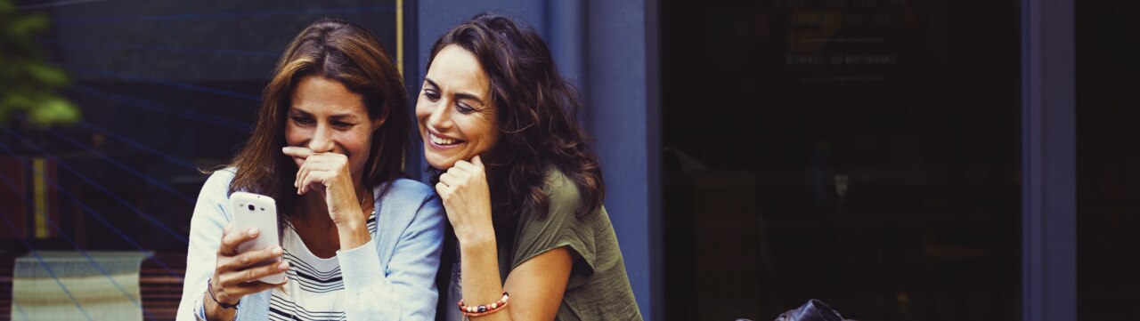 Deux femmes dans un café rient en regardant leurs smartphones