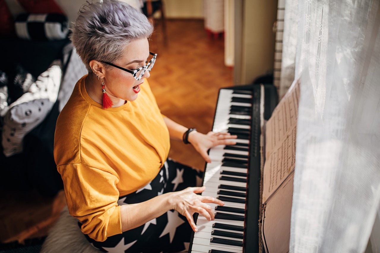 One young woman, composer, playing synthesizer and singing in living room at home.