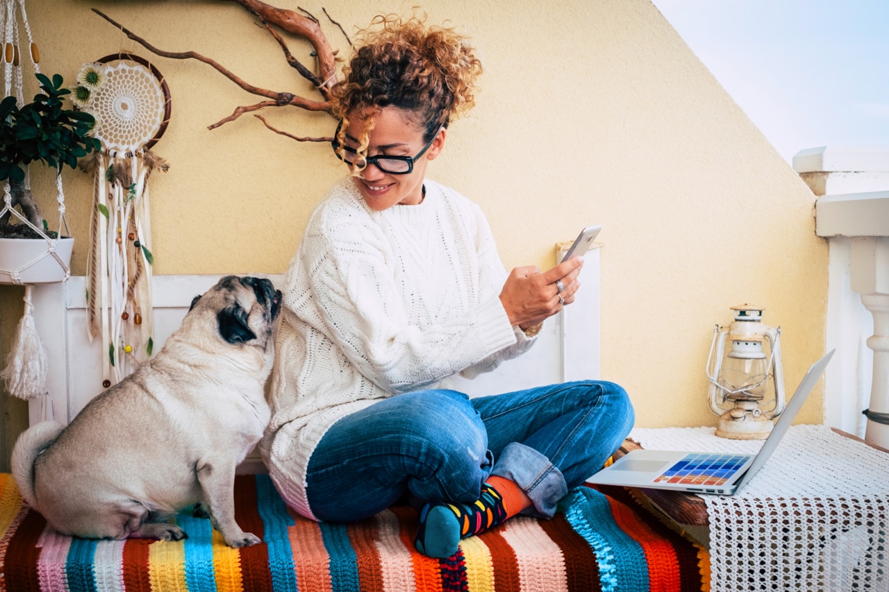 Happy couple people and animals with cheerful beautiful caucasian woman and her lovely pug dog sit down at home while work with technology devices like phone and laptop