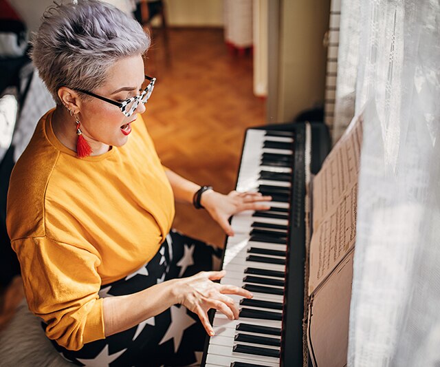 Uma mulher jovem, compositora, tocando sintetizador e cantando em uma sala em casa.