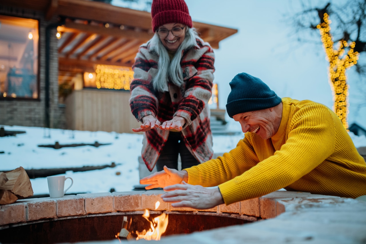 Um casal de idosos sentado e se aquecendo em uma lareira ao ar livre em uma noite de inverno.