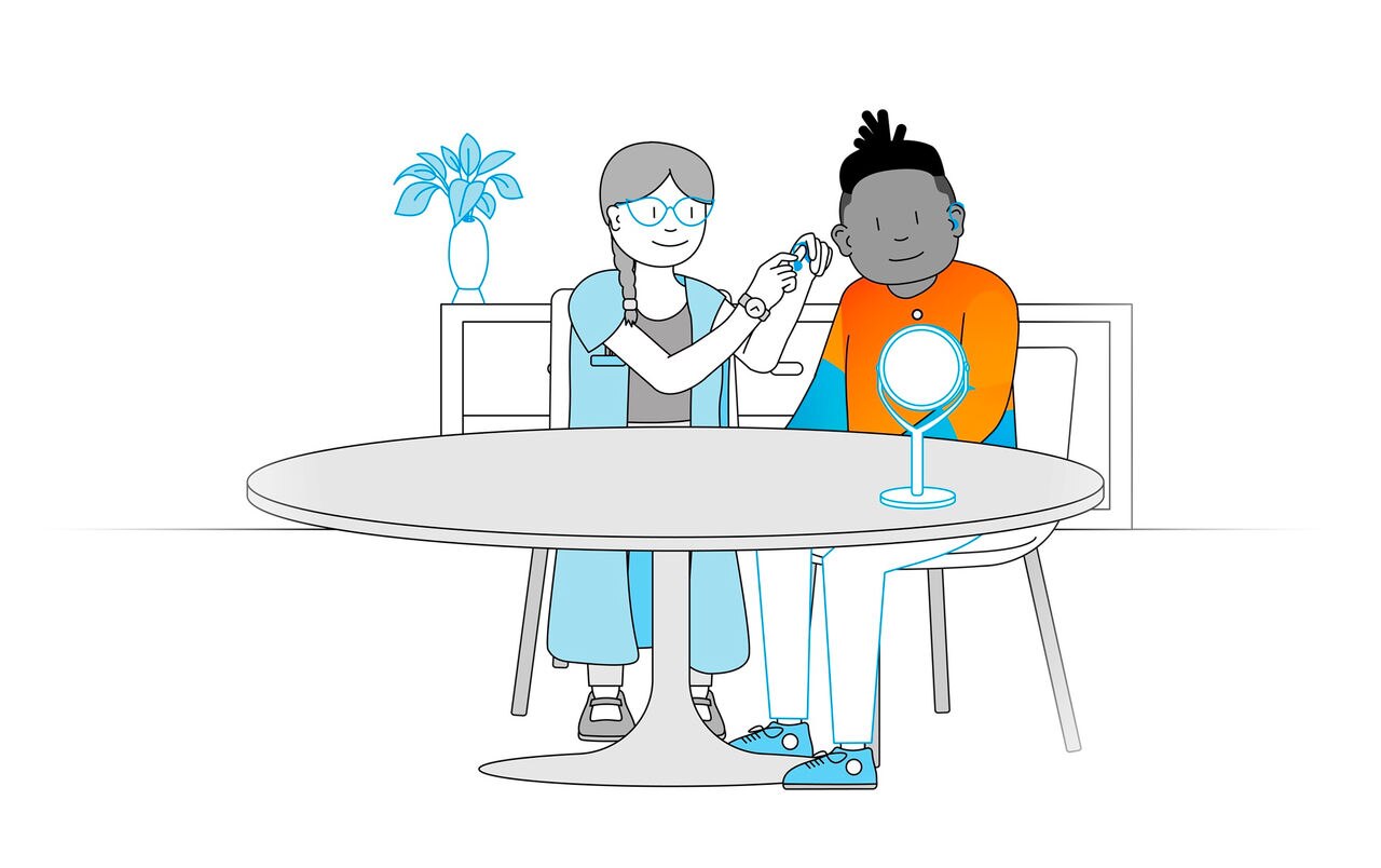 Two individuals sitting at a round table, one applying makeup to the other, with a mirror and a potted plant in the background.