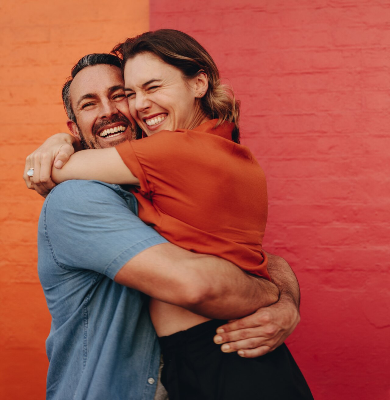 Couple d'un certain âge amoureusement enlacé devant un mur coloré. Homme et femme d'âge mûr réunis contre un mur rouge et orange.