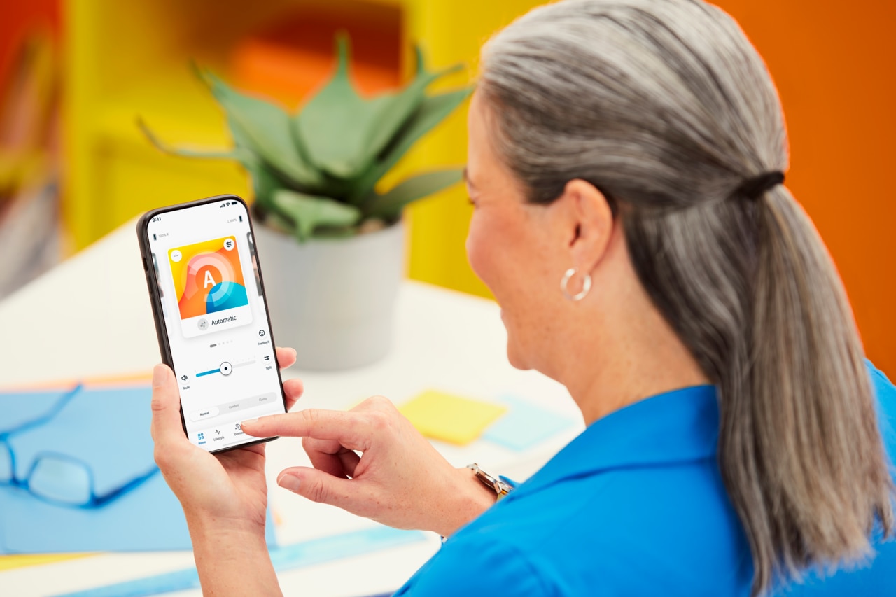 Une femme tenant un téléphone portable configure ses appareils auditifs à distance via une application.