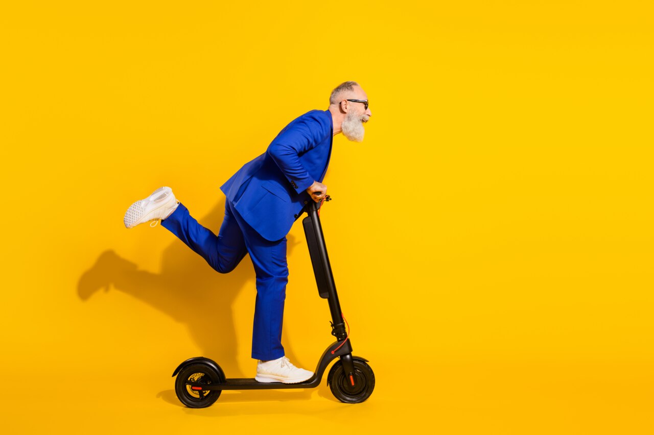 Photo de profil pleine grandeur d’un homme d'âge mûr enthousiaste conduisant un scooter sur fond jaune