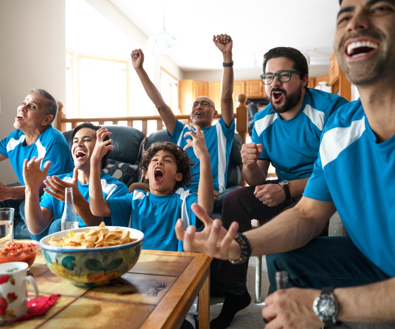 Eine lateinamerikanische Mehrgenerationenfamilie, die eine Sportsendung ansieht und sich dabei freut