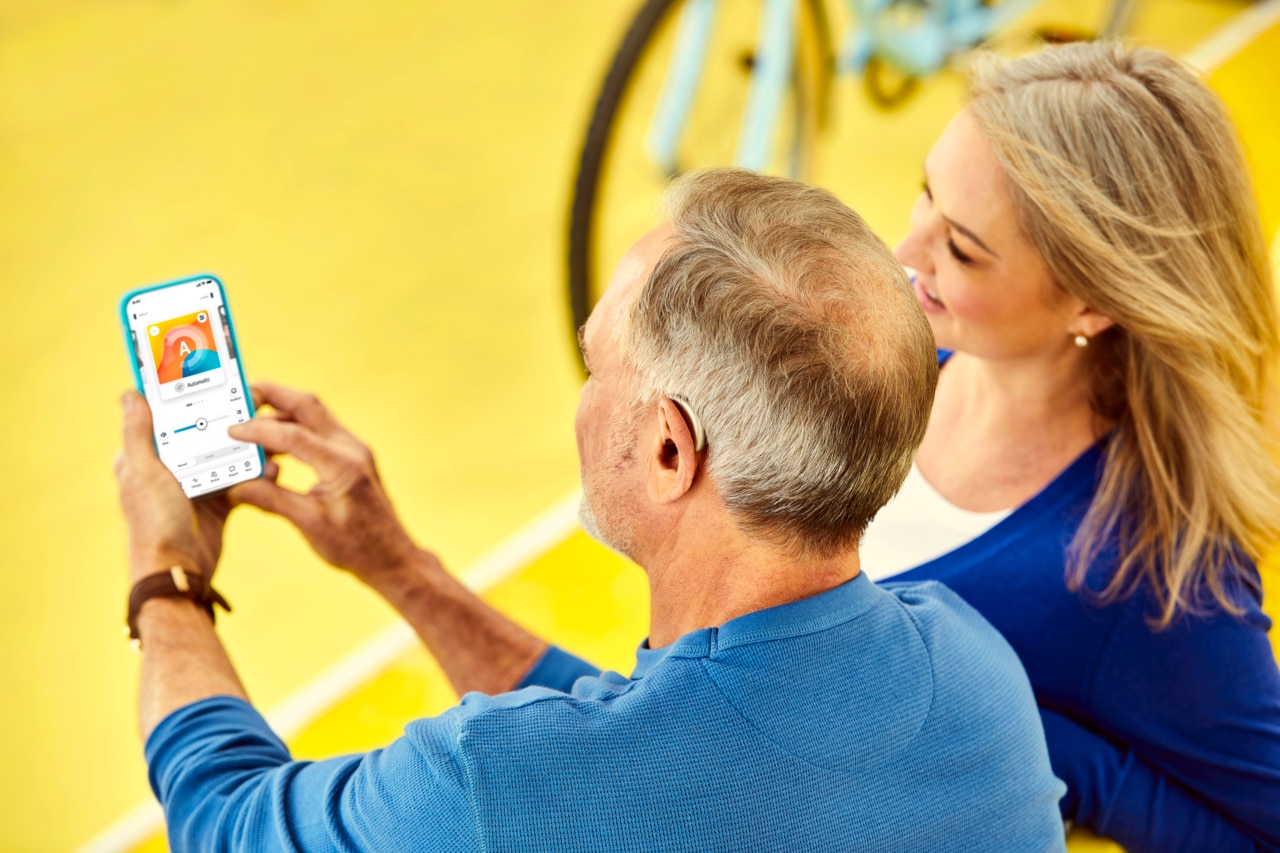 Ein Mann hält ein Mobiltelefon in der Hand und richtet sein Hörgerät über die Remote App ein