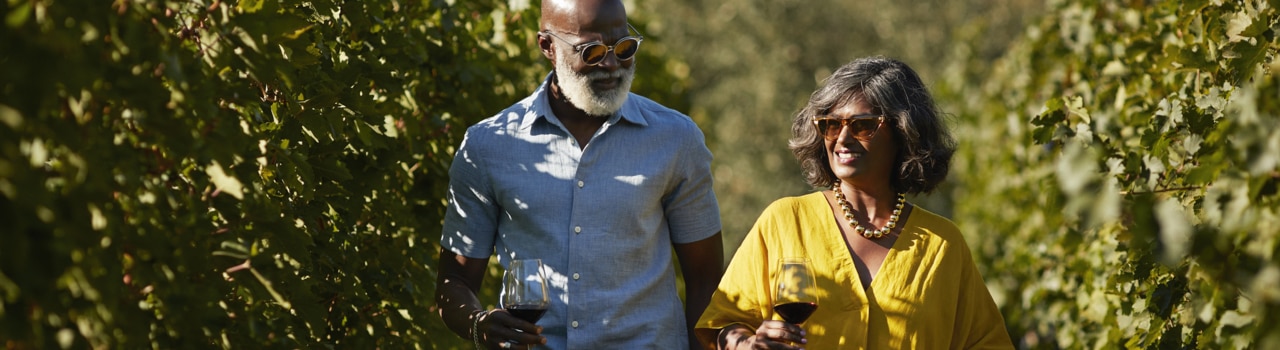 Femme mature souriante parlant à un homme âgé tout en marchant parmi les plantes dans le vignoble