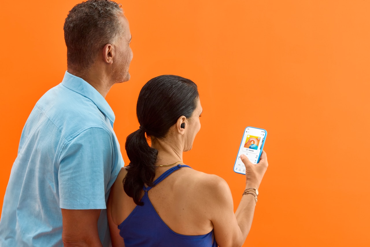 Une femme tenant un téléphone portable, réglant ses aides auditives au moyen d’une application à distance