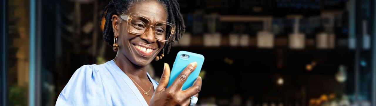 Afroamerikanische Frau lächelt, während sie auf ein Telefon schaut