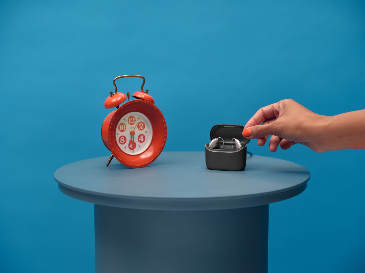 Ein Paar Vivante Hörgeräte in einer Ladestation, die auf einem Tisch neben einer großen roten Weckeruhr steht