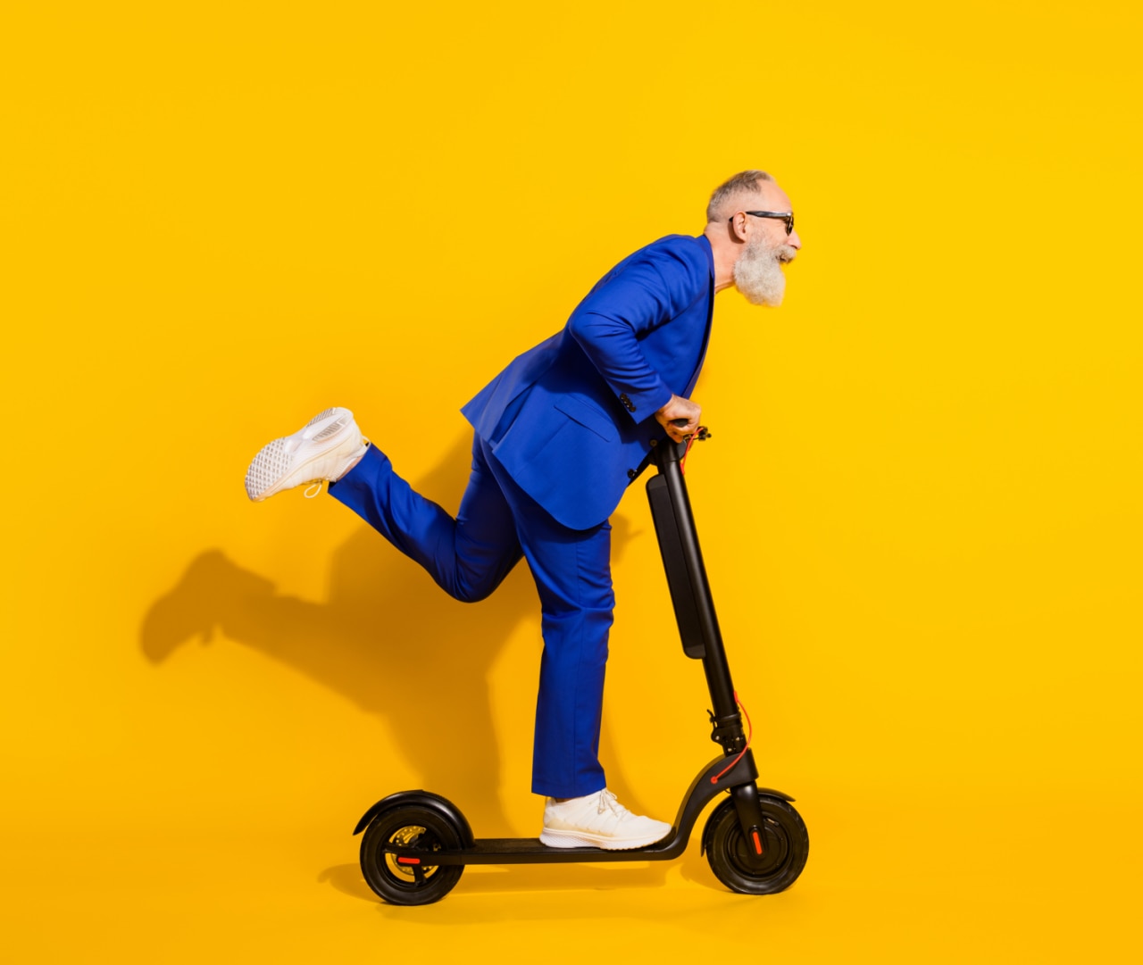 Foto de perfil de tamaño completo de un hombre maduro feliz y emocionado, con expresión divertida, con espacio para texto, montando un monopatín, solo sobre un fondo de color amarillo