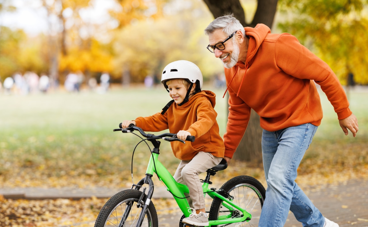 An elderly man is seen helping a child ride his bike