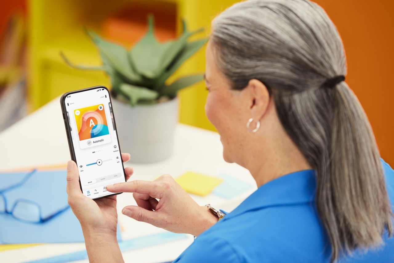 A woman holding a mobile phone, setting up her hearing aids via remote app