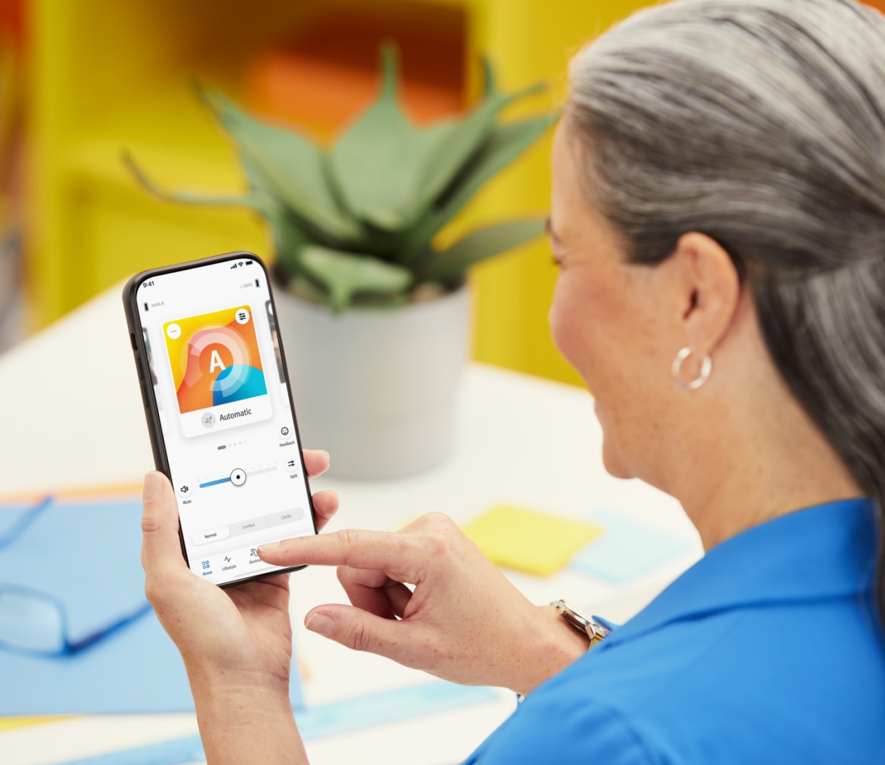 A woman holding a mobile phone, setting up her hearing aids via remote app