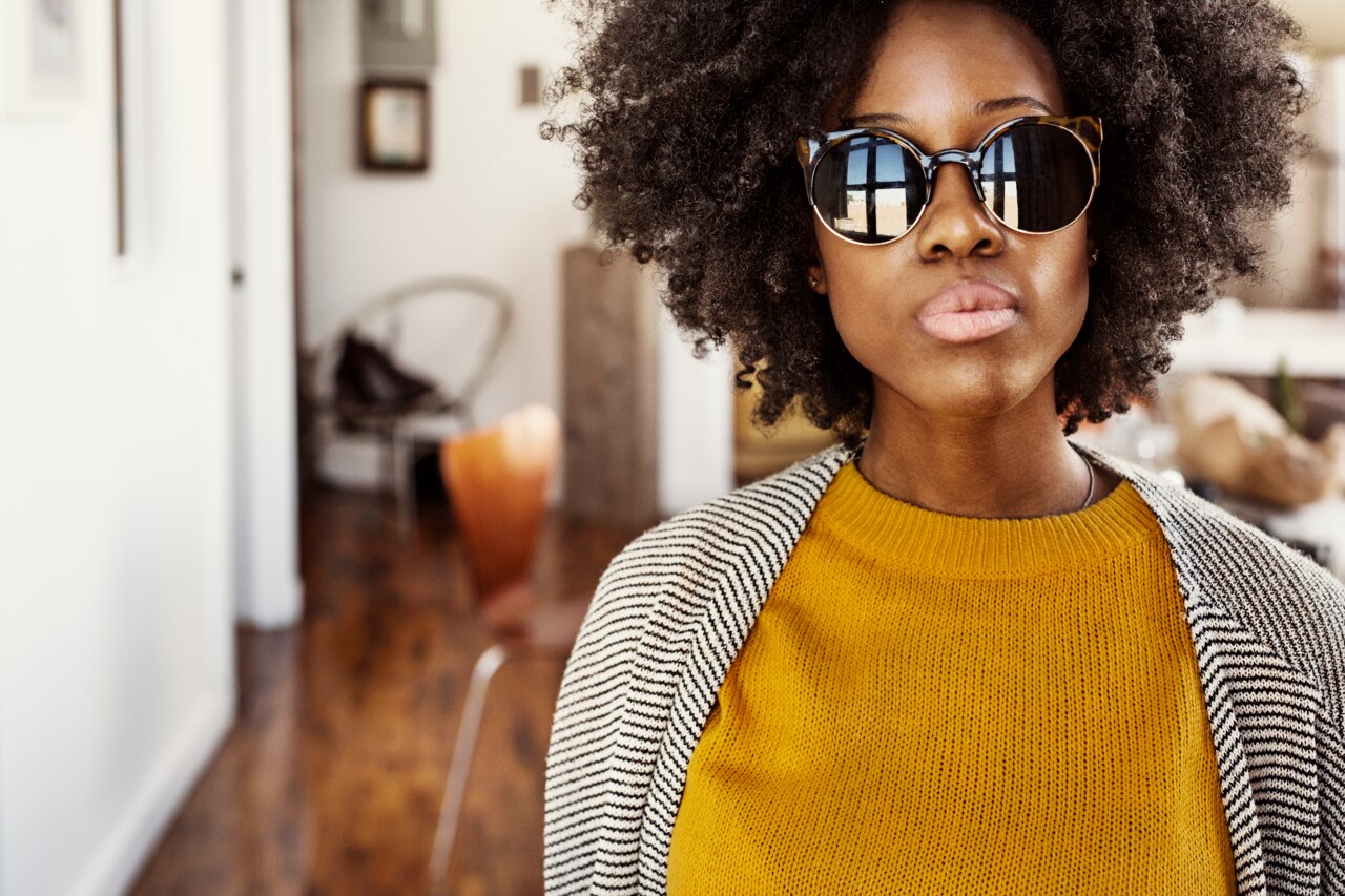 A person is wearing a cozy yellow sweater paired with a striped cardigan, standing in a bright, inviting indoor space. The background features wooden flooring and a glimpse of modern furniture