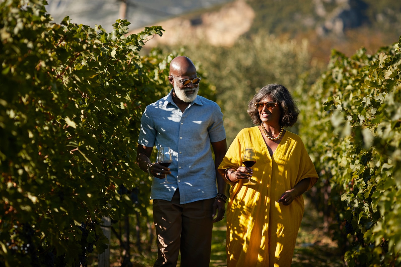 Smiling mature woman talking to senior man while walking amidst plants in vineyard