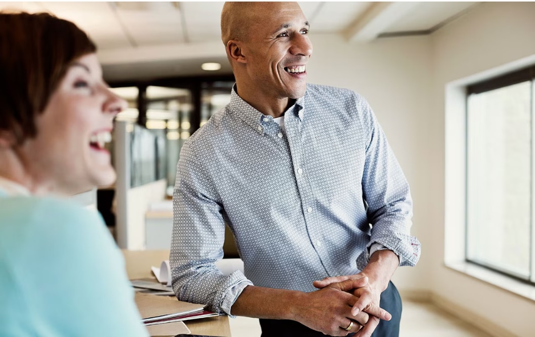 A woman an a man standing in a brightly lit office, chatting and smiling
