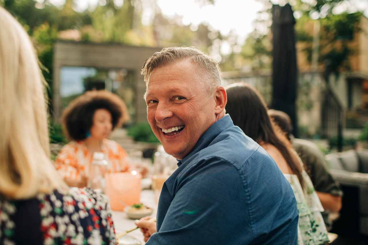 A man smiling at the camera, eating dinner with friends, celebrating, having good time