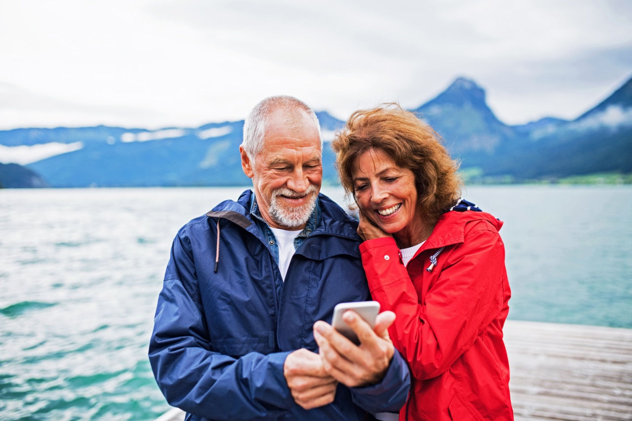  a couple standing close together by a body of water, likely a lake, with mountains in the background.