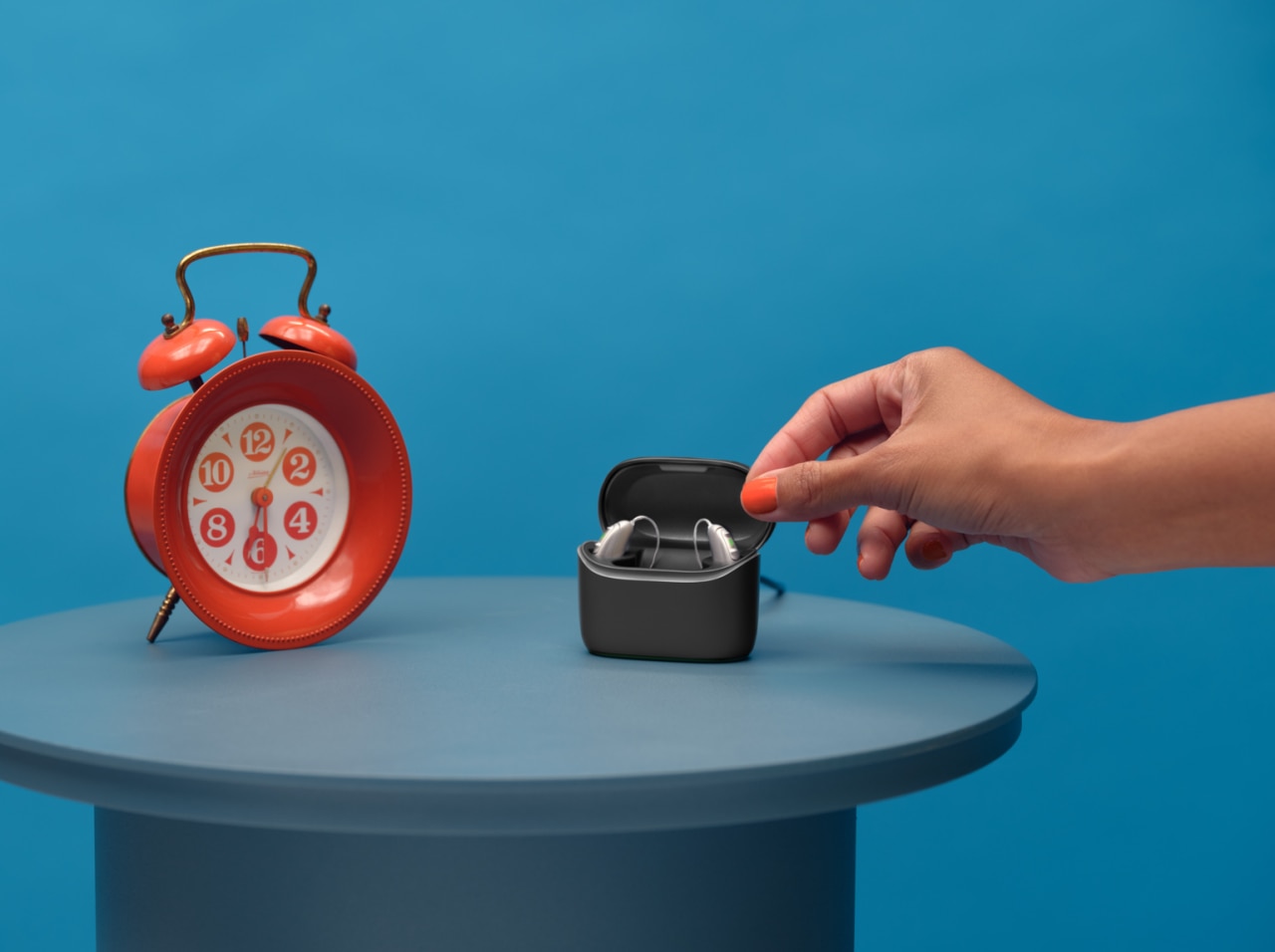 A pair of Vivante hearing aids in a charger standing on a table next to a big red alarm clock