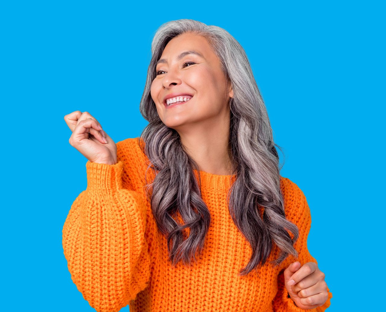 Elderly woman with grey hair smiling in an orange sweater.