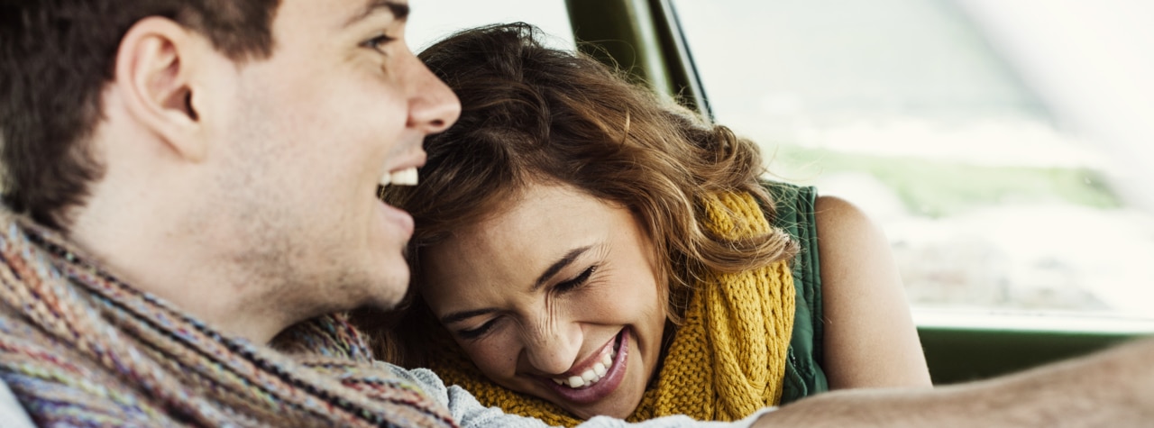 A smiling couple inside a car, enjoying a moment together.