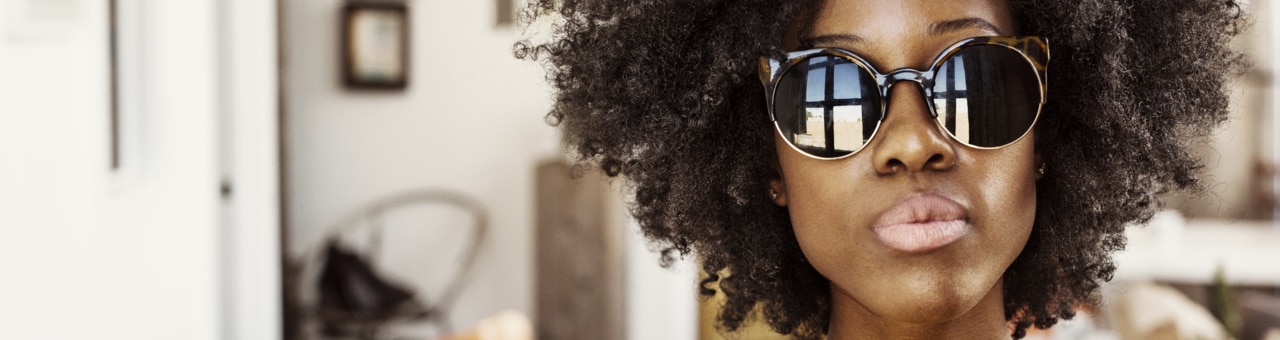 A person is wearing a cozy yellow sweater paired with a striped cardigan, standing in a bright, inviting indoor space. The background features wooden flooring and a glimpse of modern furniture